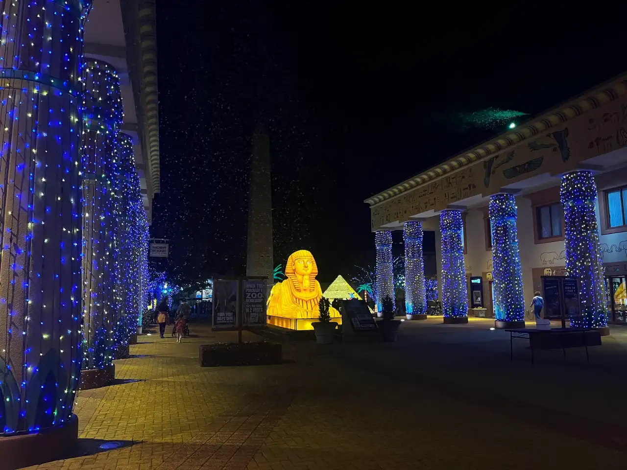 Commercial plaza with tall columns wrapped in blue and white lights at night