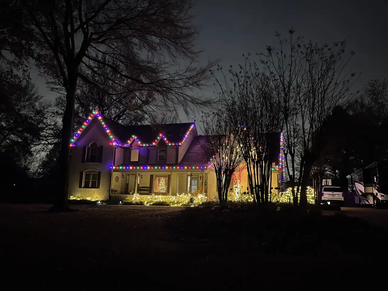 Two-story home with purple and multicolor roofline lights and warm white shrubs at night