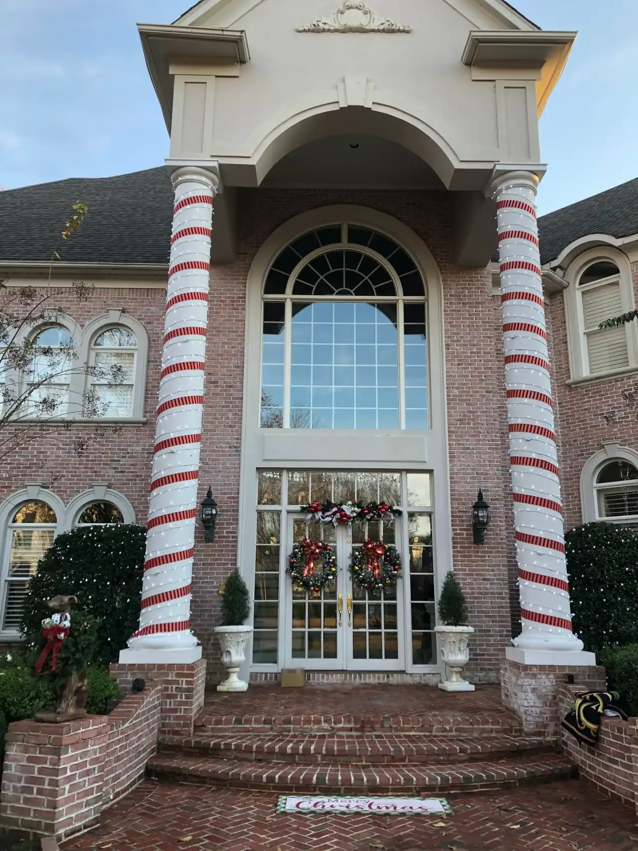 Porch columns wrapped in red and white with wreaths and garland on the front doors